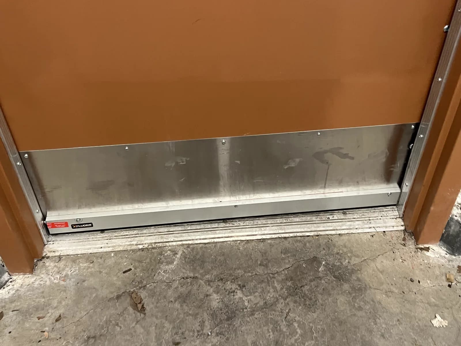 A stainless rodent-proof door sweep installed at the base of a door