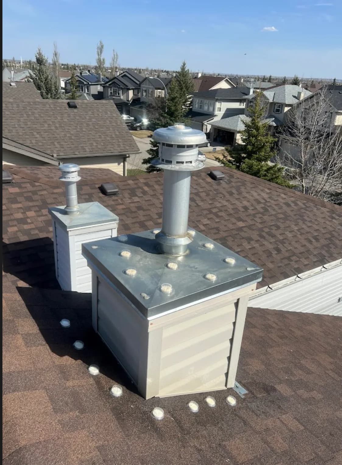Two custom sheet-metal chimney caps above a suburban neighbourhood