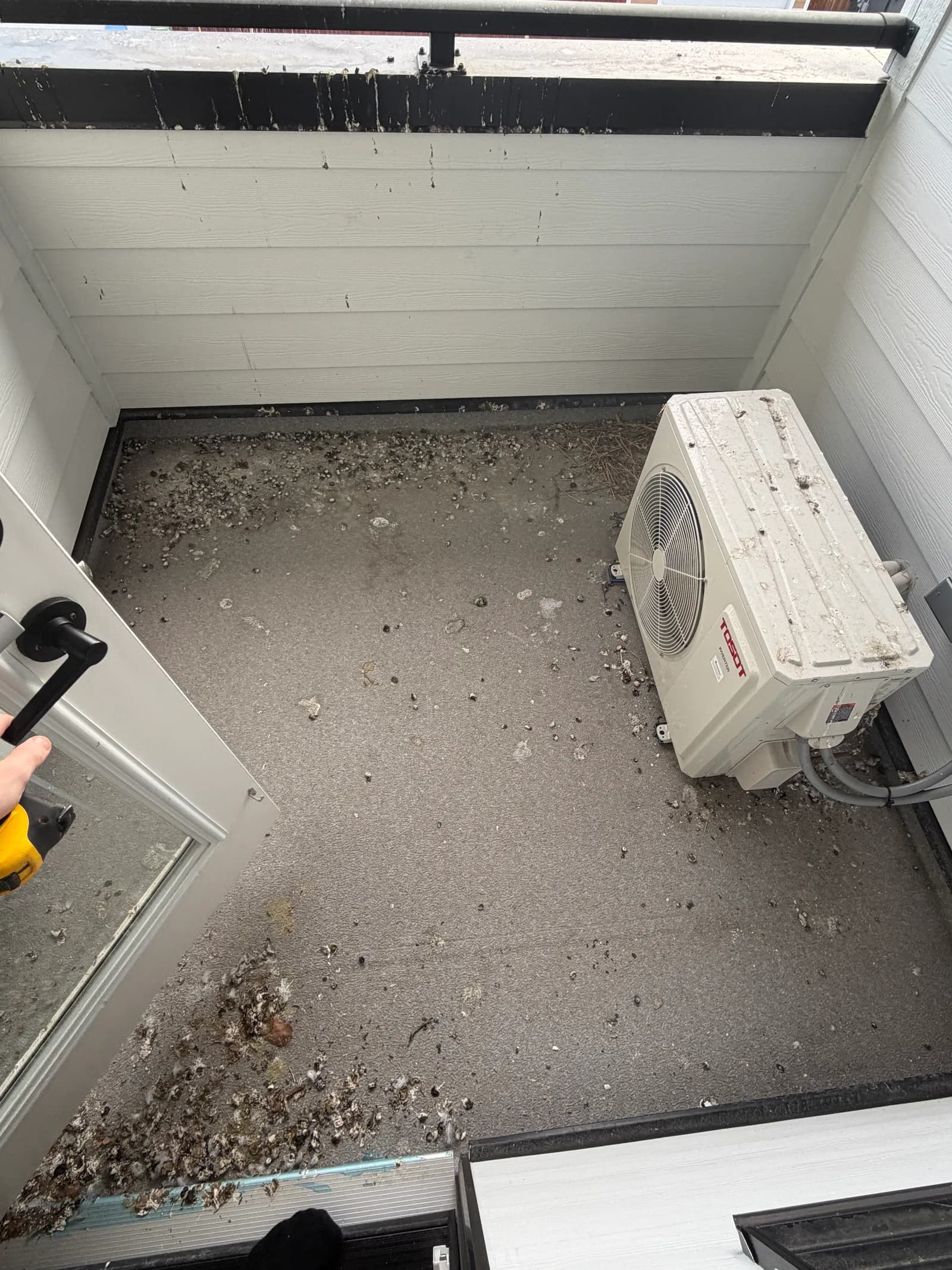 A balcony floor being cleared of pigeon droppings around an AC unit